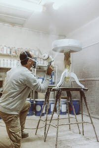 Männlicher Arbeiter, der in einer Werkstatt einen Tisch mit einer Spritzpistole lackiert - OCAF00575