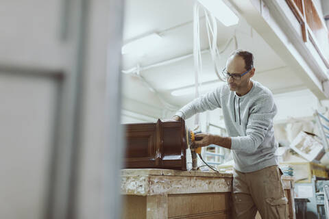 Craftsman using sander on furniture while standing at workshop stock photo