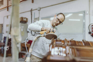 Male expertise polishing furniture with sander while standing at workshop - OCAF00581