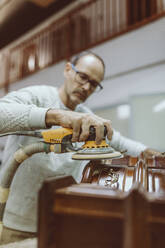 Craftsman using sander for polishing while working at workshop - OCAF00582
