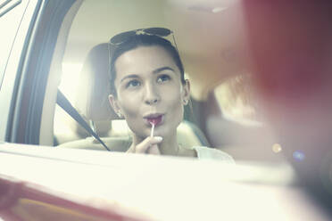 Young woman licking lollipop while day dreaming in car during road trip - AJOF00817