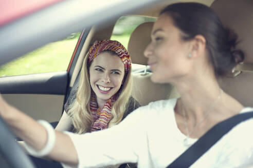 Lächelnde Freunde, die sich im Auto auf einer Autoreise unterhalten - AJOF00821
