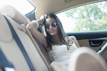 Junge Frau mit cooler Einstellung lehnt sich auf dem Rücksitz während einer Autofahrt - AJOF00823