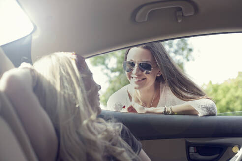 Junge Frau lehnt sich an ein Autofenster und spricht mit einem Freund während einer Autofahrt - AJOF00824