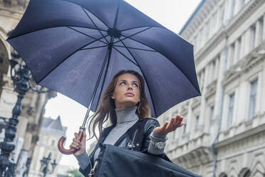 Geschäftsfrau, die während der Regenzeit in der Stadt unter einem Regenschirm wegschaut - AJOF00830