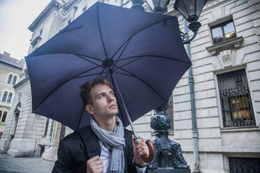 Nachdenklicher Geschäftsmann unter Regenschirm während der Regenzeit - AJOF00834