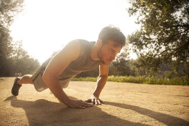 Athlete exercising while doing push-ups on footpath - AJOF00849