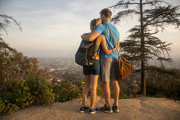 Paar, das sich umarmt, während es auf einem Berg stehend die Aussicht betrachtet - AJOF00856