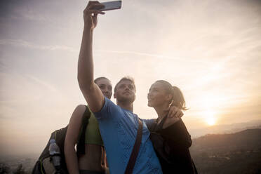 Lächelnde Freunde nehmen Selfie durch Handy, während gegen den Himmel stehen - AJOF00858