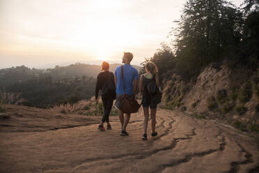 Friends with bag walking together on mountain path during sunset - AJOF00859