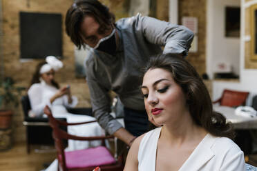 Älterer männlicher Friseur bei der Vorbereitung der Braut auf die Hochzeit während COVID-19 - EGAF01106