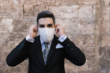 Young groom wearing protective face mask against wall - EGAF01149