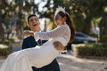 Lachende Braut mit Bräutigam im Park an einem sonnigen Tag - EGAF01168