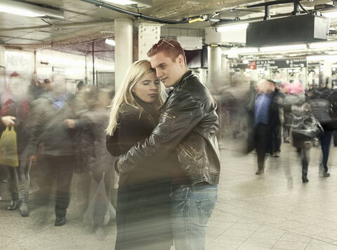 Young couple embracing each other while standing at subway station during rush hour stock photo