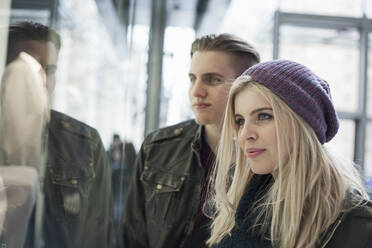 Girlfriend wearing knit hat doing window shopping while standing with boyfriend by store window - AJOF00872