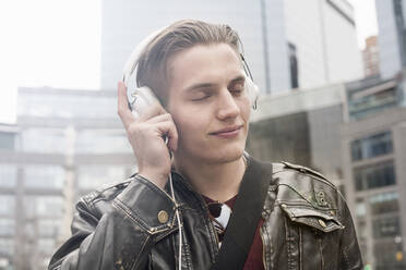 Mann mit geschlossenen Augen hört Musik, während er in der Stadt steht - AJOF00887