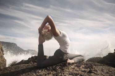 Flexible Frau beim Üben von Sirsapada Natarajasana auf einer Felsformation - AJOF00899