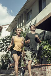 Junger Mann und Frau laufen zusammen an einem sonnigen Tag die Straße entlang - AJOF00945
