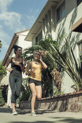 Female friends talking while jogging on sidewalk during sunny morning - AJOF00946