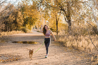 Cheerful woman walking with her dog at countryside on sunny day - MRRF00709