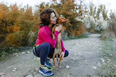Mittlere erwachsene Frau sieht ihren Hund an, während sie auf einem Weg in der Landschaft kauert - MRRF00714