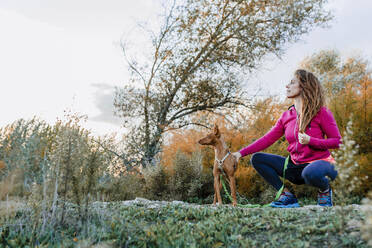 Frau mit braunen Haaren mit ihrem Hund, der in die Landschaft schaut - MRRF00715