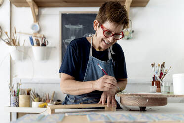 Smiling owner painting craft product in ceramic workshop - EGAF01172