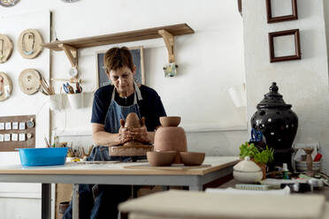 Ältere Künstlerin, die in einem Keramikgeschäft aus braunem Ton töpfert - EGAF01181