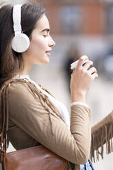 Junge Frau mit Kopfhörern hört Musik und hält einen Einwegbecher - GGGF00252