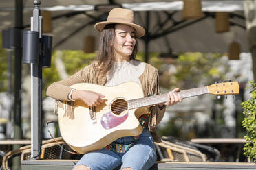 Smiling young woman playing guitar on sunny day - GGGF00256