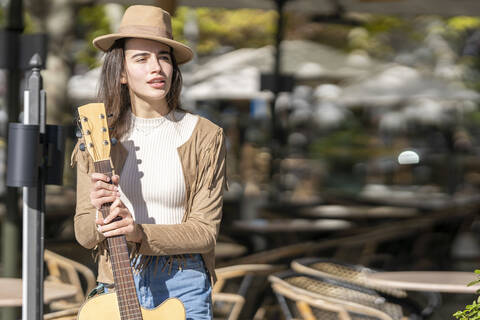 Thoughtful young woman with guitar standing during sunny day stock photo