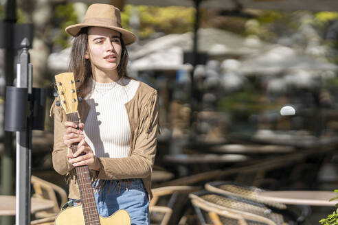 Nachdenkliche junge Frau mit Gitarre an einem sonnigen Tag - GGGF00257