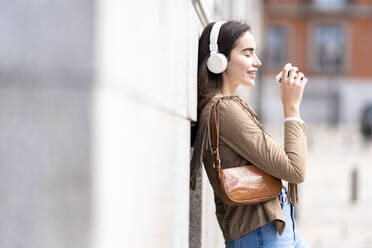 Young woman holding coffee cup while leaning on wall - GGGF00275