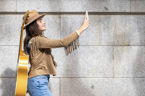 Young female musician taking selfie while walking by wall stock photo