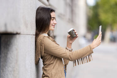 Lächelnde junge Frau, die ein Selfie macht, während sie sich an die Wand lehnt - GGGF00295