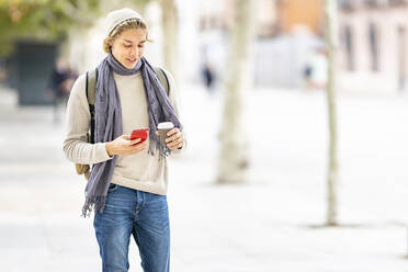 Junger Mann mit Kaffeetasse und Mobiltelefon in der Stadt stehend - GGGF00318