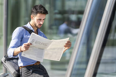 Junger Geschäftsmann liest im Freien sitzend Zeitung - GGGF00346