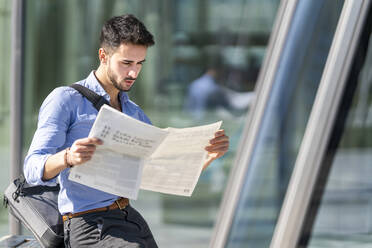 Young businessman reading newspaper while sitting outdoors - GGGF00346