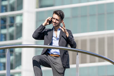 Junger Geschäftsmann lächelt, während er im Freien mit dem Handy spricht - GGGF00376