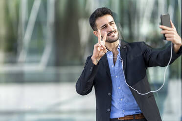 Confident businessman showing peace sign while taking selfie - GGGF00378