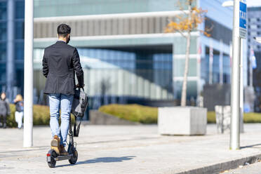 Businessman riding push scooter on footpath - GGGF00384