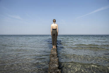 Frau schaut auf das Meer, während sie auf einer hölzernen Buhne in Mecklenburg, Fischland-Darß-Zingst, Deutschland, steht - CHPF00719