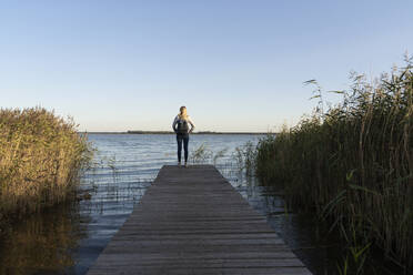 Tourist mit Rucksack, der das Meer bewundert, während er auf dem Bootssteg in Mecklenburg, Fischland-Darß-Zingst, Deutschland, steht - CHPF00723