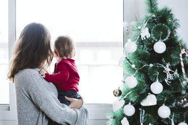 Mutter mit kleinem Jungen schaut durch das Fenster, während sie zu Hause in der Weihnachtszeit steht - EBBF01692