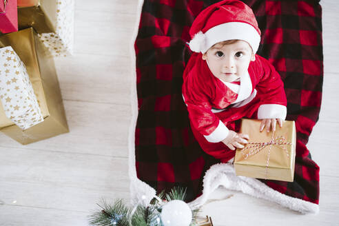 Süßes Baby in Santa Claus Kostüm spielen mit Geschenk-Box, während zu Hause sitzen während Weihnachten - EBBF01704