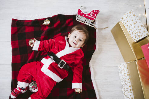 Lächelnder kleiner Junge im Weihnachtsmannkostüm, der zu Hause auf einer Decke liegt, während Weihnachten - EBBF01707