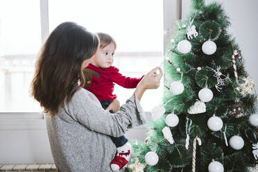 Mutter zeigt dem kleinen Jungen zu Hause während der Weihnachtszeit eine Dekoration - EBBF01708