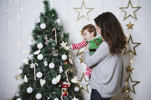 Mother carrying son while standing by tree at home during Christmas stock photo