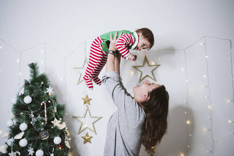 Lächelnde Frau, die einen kleinen Jungen beim Spielen zu Hause abholt, während Weihnachten, lizenzfreies Stockfoto