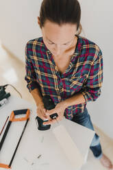 Woman changing drill bit of electric drill while standing at home - DMGF00398